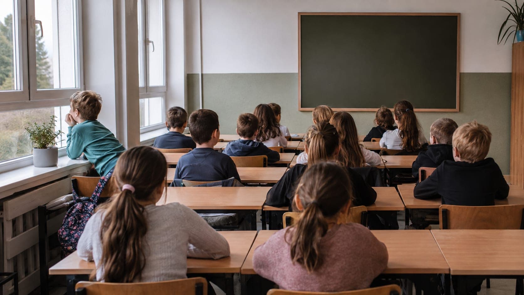 Klasa siedzi zwrócona do tablicy, jedno dziecko przy oknie patrzy na zewnątrz Klasa siedzi zwrócona do tablicy, jedno dziecko przy oknie patrzy na zewnątrz