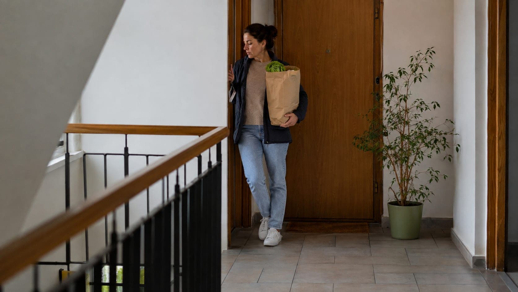 Kobieta z torbą zakupów stoi na klatce schodowej przy drzwiach mieszkania Kobieta z torbą zakupów stoi na klatce schodowej przy drzwiach mieszkania